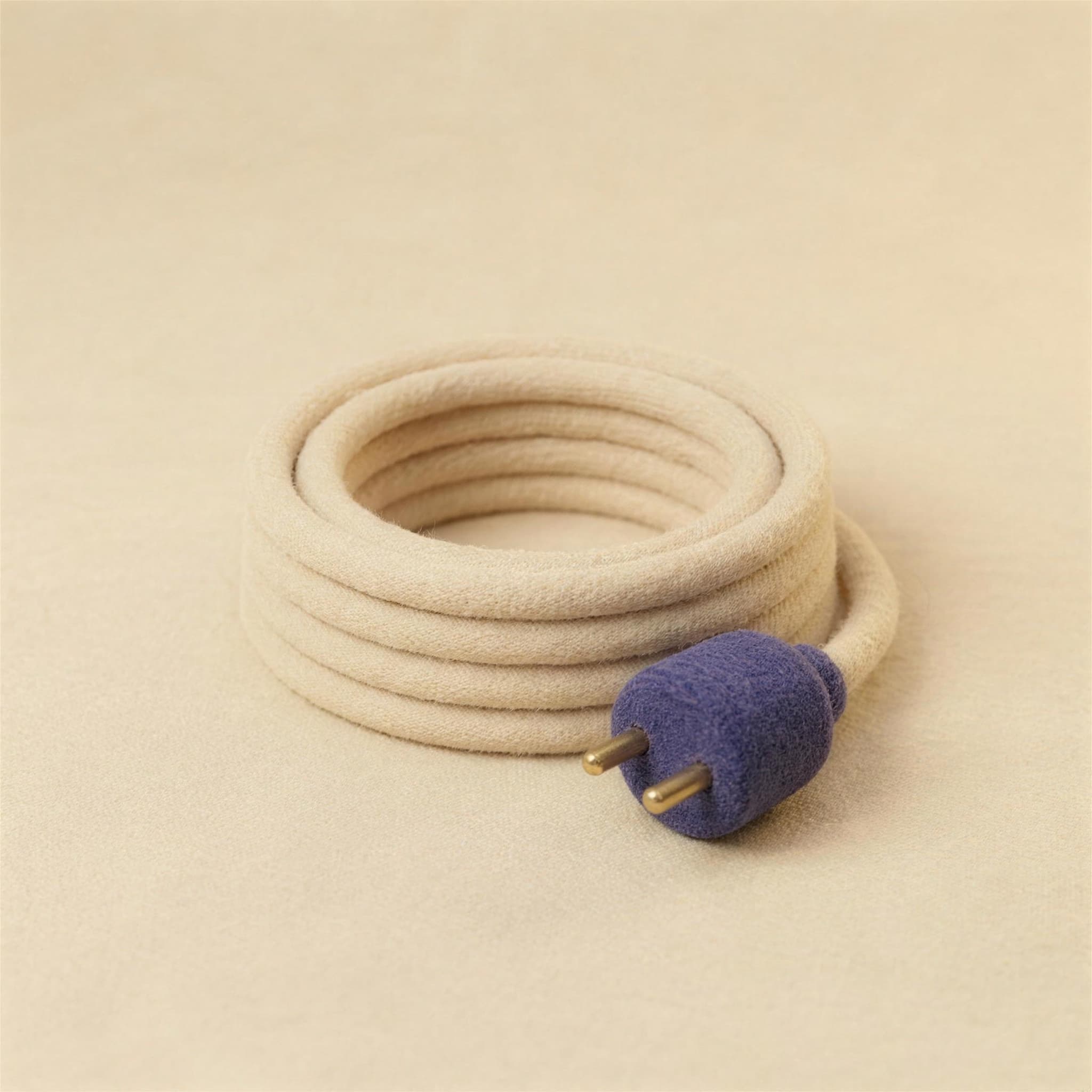 A neatly coiled cream felt cable ending in an indigo plug